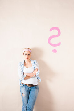Studio Shot of Young Woman Leaning Against Wall with Question Mark