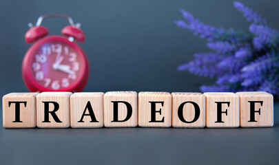 TRADEOFF - word on wooden cubes on a gray background with an alarm clock and a branch of lavender