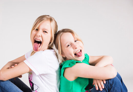 Portrait of Girls Sitting Back to Back and Sticking their Tongues Out
