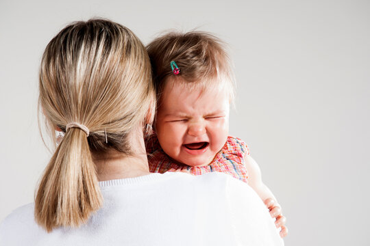 Over the Shoulder View of Mother holding Crying Baby Girl, Studio Shot