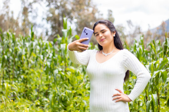 Retrato de una hermosa chica tomándose fotos en un parque,mujer feliz revisando teléfono inteligente en aire libre,chica usando el móvil en medio de un camino rodeado de montañas