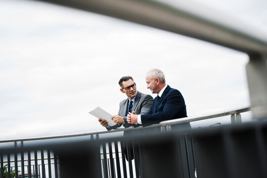 Mature businessmen standing on bridge talking, Mannheim, Germany