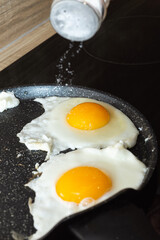 Salting of fried eggs in a frying pan on electric stove portrait view