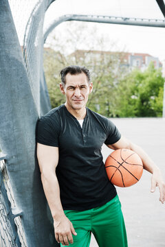 Portrait of mature man standing on outdoor basketball court, Germany