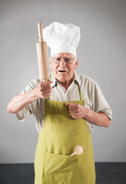Elderly Man wearing Apron and Chef's Hat holding Rolling Pin in Studio