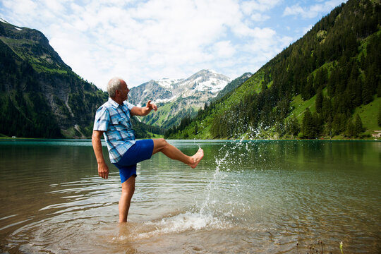 Mature man standing in lake, kicking water, Lake Vilsalpsee, Tannheim Valley, Austria