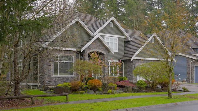 Establishing shot of two story stucco luxury house with big tree and nice landscape at spring rainfall in Vancouver, Canada, North America. Day time on April 2023. ProRes 422 HQ.