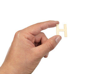 Close up of a person's hand holding a small wooden letter H isolated on a white background