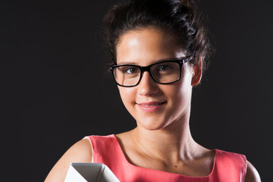 Close-up portrait of teenage girl wearing horn-rimmed eyeglasses, holding binder, smiling and looking at camera