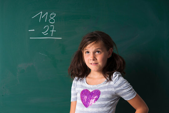 Portrait of girl standing in front of blackboard in classroom, Germany