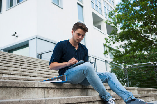 Young man sitting on steps outdoors, using tablet computer, Germany