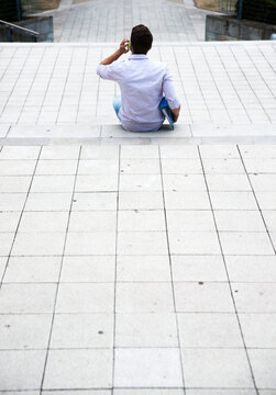 Backview of young man sitting on steps outdoors, using cell phone, Germany