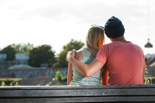 Backview of teenage boy with arm around teenage girl, sitting on bench outdoors, Germany