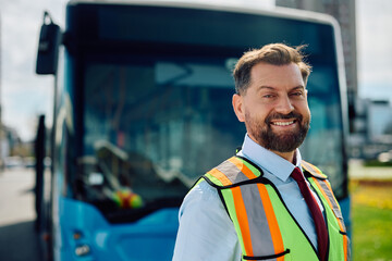 Happy bus driver in front of vehicle looking at camera.