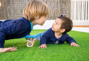 Picture of brother and sister having fun in the park, two cheerful children laying down on green grass, little girl and boy playing outdoors, best friends, happy family, love and happiness concept