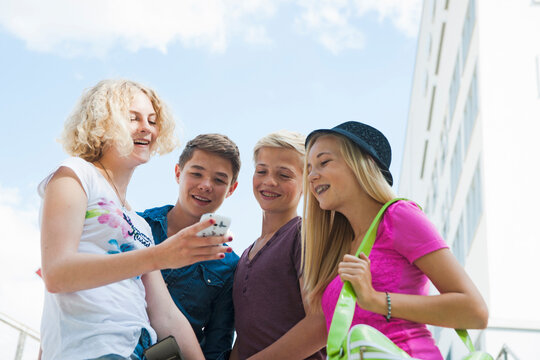 Group of teenagers standing outdoors looking at cell phone and talking, Germany