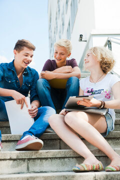 Teenagers sitting on stairs outdoors, talking and looking at tablet computer, Germany