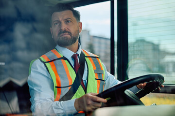 Professional driver looking at rear view mirror while driving a bus.