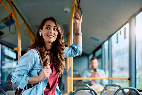 Young smiling woman holds onto handle while traveling by public bus.