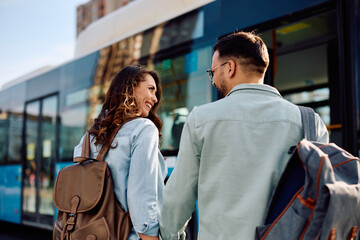 Rear view of happy tourist couple at bus station.