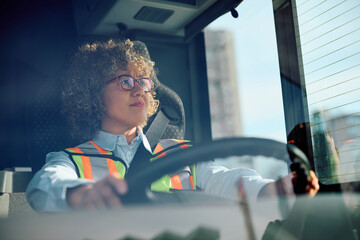 Female bus driver driving in reverse while looking in side view mirror. - obrazy, fototapety, plakaty