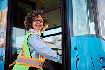 Happy female bus driver entering in vehicle and looking at camera.