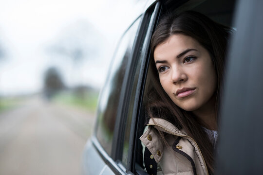 Portrait of young woman sitting inside car and looking out of window and day dreaming on overcast day, Germany