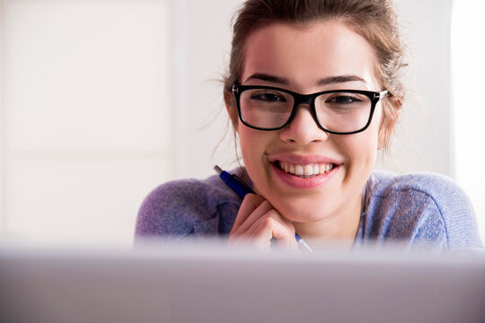 Close-up portrait of young woman with laptop computer wearing eye glasses, smiling and looking at camera, studio shot