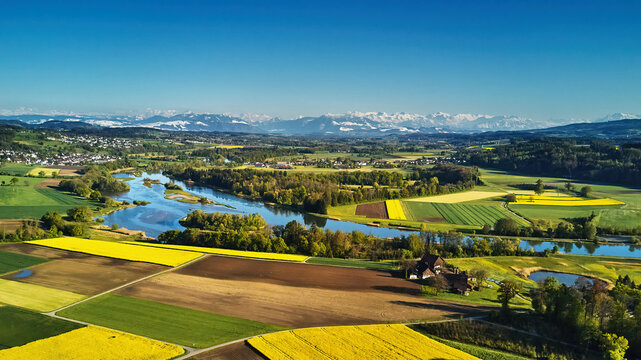 Blick &uuml;ber den Flachsee (Reuss) umgeben von einem bunten Mosaik aus Wald, Wiesen, Rapsfeldern und Ackerfl&auml;chen, die sich bis zu den Bergen hinziehen. Wolkenloser, stahlblauer Himmel..