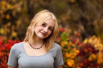 Portrait of a beautiful young teenage woman against a forest background in a city park on a warm fall day; St. Albert, Alberta, Canada