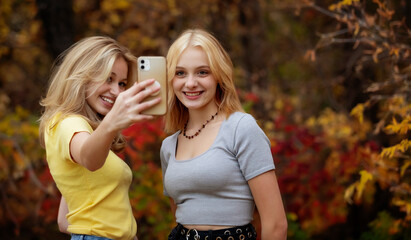 Two teenage girls taking self-portraits with a smart phone while spending time together in a city park on a warm fall day; St. Albert, Alberta, Canada.
