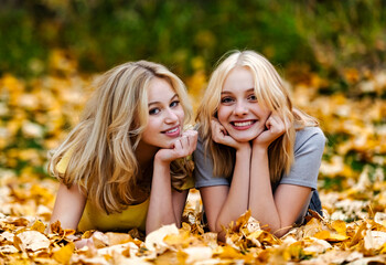 Portrait of two teenage girls laying in the leaves and posing for the camera in a city park on a warm fall afternoon; St. Albert, Alberta, Canada.