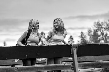 Black and white image of two teenage girls standing on a bridge spending quality time together in a city park; St. Albert, Alberta, Canada.
