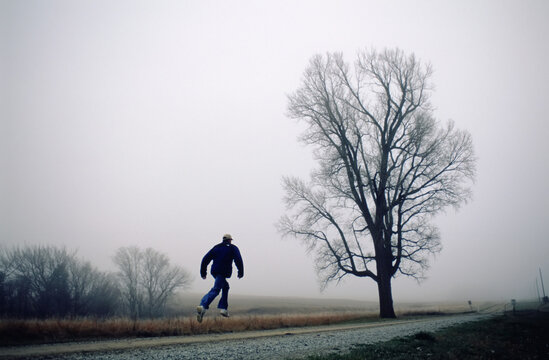 Young man leaps in the air on a gravel road in the countryside on a foggy day; Walton, Nebraska, United States of America