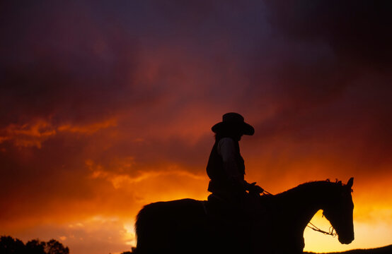 Silhouette of a cowboy riding horseback at sunrise with a dramatic sky; Santa Fe, New Mexico, United States of America