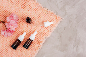 Brown glass bottles with essential oil and pink cherry blossom on a towel on gray concrete background. Skin care, beauty treatment concept. Top view, flat lay