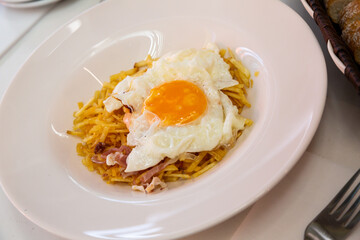 Traditional appetizing spanish lunch - fried egg with french fries and slices of jamon on white plate