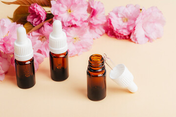 Brown glass bottles with essential oil and pink cherry blossom on beige background. Aromatherapy,...