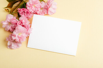 Blank card and cherry blossom on beige background. Top view, mockup