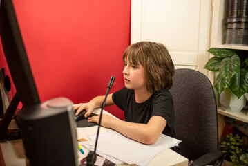 the child is sitting at the table, in front of the computer, studying the material of the online...