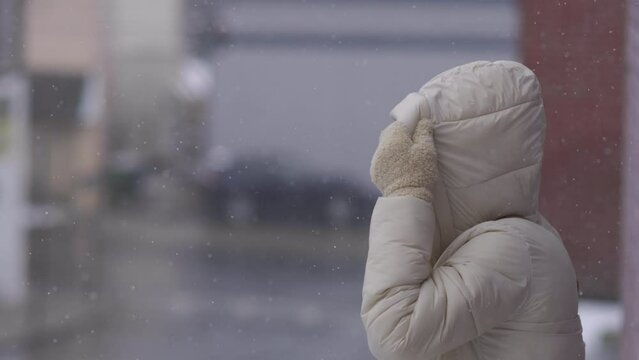 A woman pulls up her parka's hood while standing in the snowy outdoors