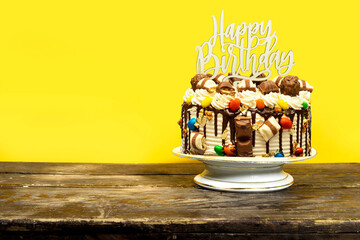 Birthday layer cake decorated with chocolate pieces with happy birthday text on stand cake on wooden board 