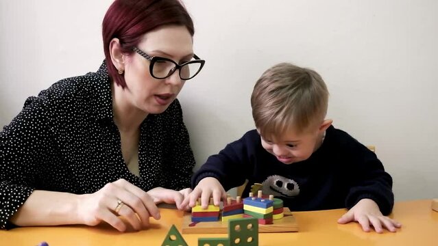 cute kid with special needs playing with developing toys in daycare rehab center.Teacher help him to develope playing educational games.