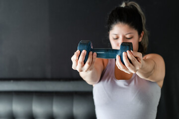 Fototapeta na wymiar young latina woman very concentrated lifting a blue dumbbell, working her muscle endurance.