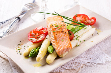 Traditional German green and white asparagus with salmon and tomatoes served as close-up on a design plate