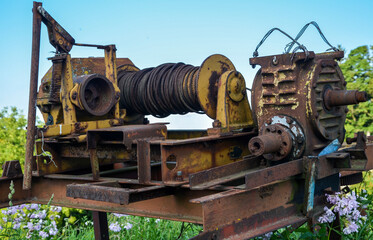 Old rusty metal Winch with electric motor, coiled rope and traces of yellow paint in the middle of green grass
