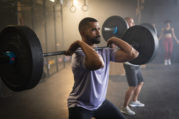 Dedicated biracial bearded young man lifting barbell while standing in gym