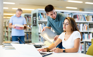 Obraz premium Friendly young woman offering assistance to male friend studying, finding information at university library