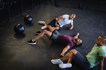 High angle view of biracial male friends relaxing on floor and talking in gym, copy space