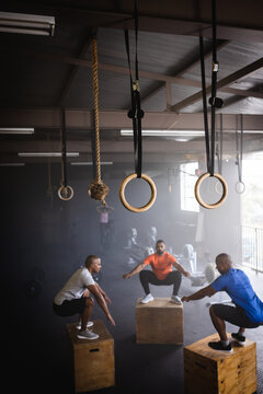 Biracial male friends practicing squats on wooden boxes in gym, copy space
